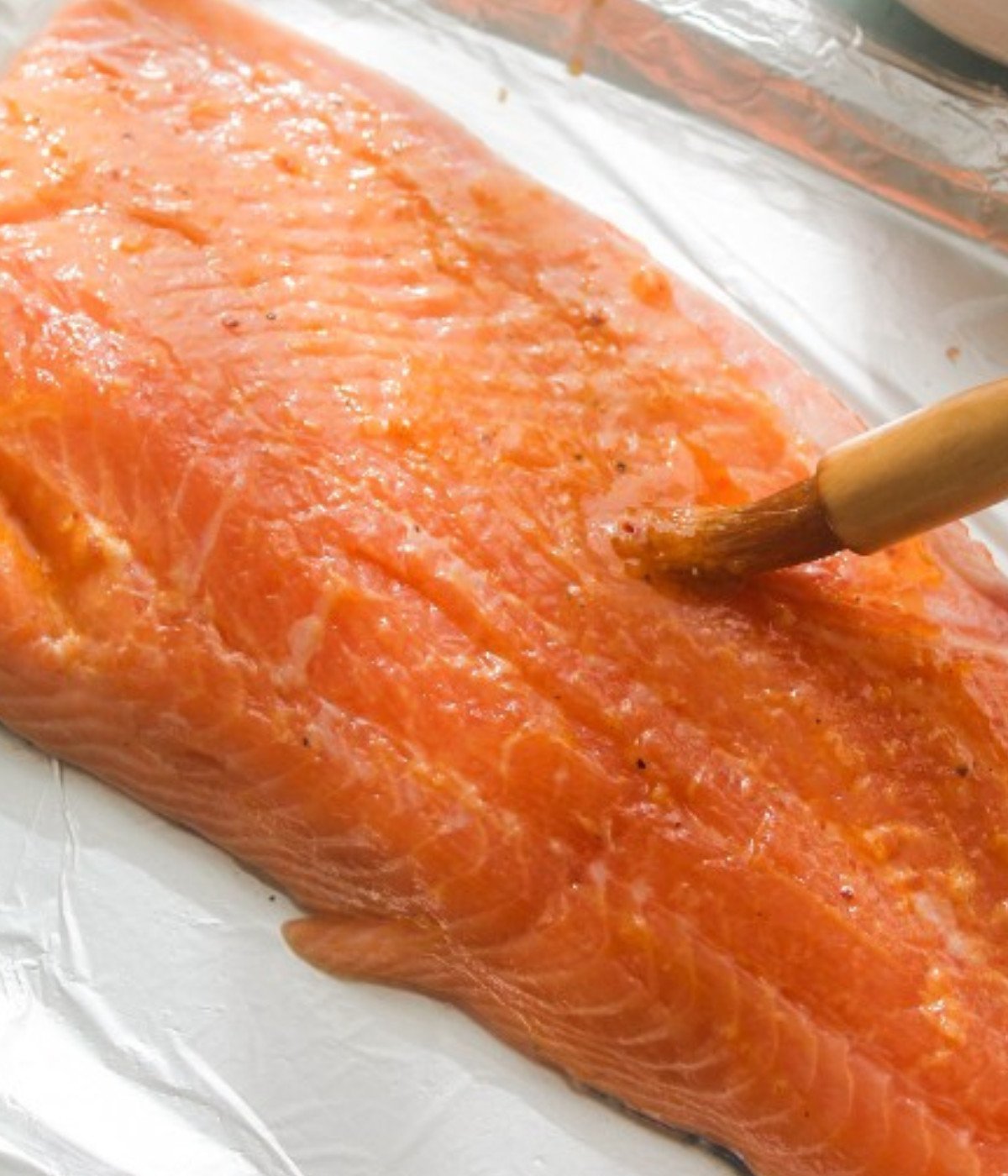 Raw salmon fillet on a baking tray lined with foil basted with lemon marinade.