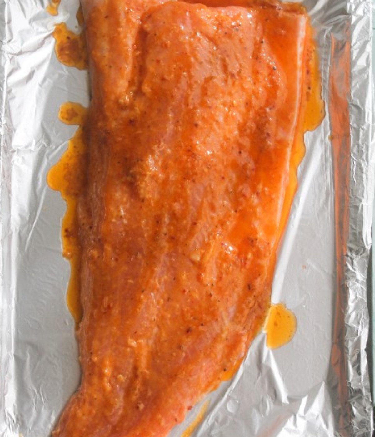 Raw salmon fillet on a baking tray lined with foil marinated.