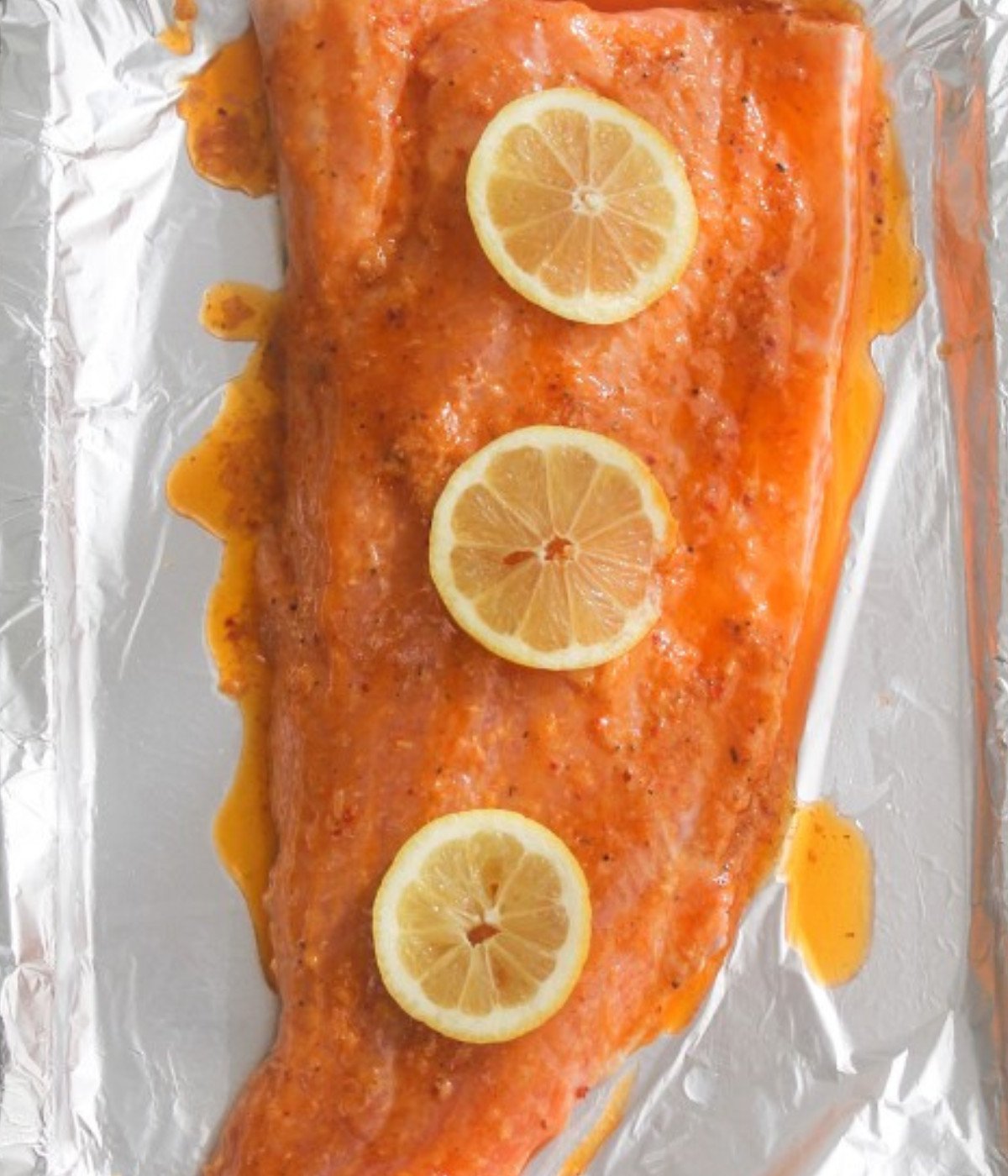 Salmon fillet on a baking tray lined with foil marinated topped with three lemon slices.
