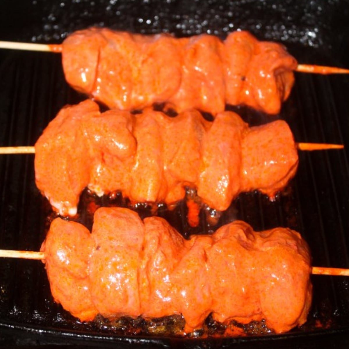 Tandoor chicken skewers cooking on a grill.