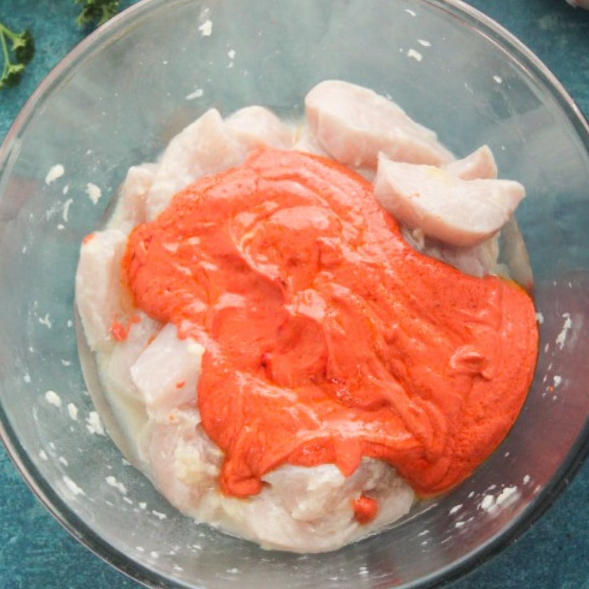 Tandoori marinade and chicken in a glass bowl.