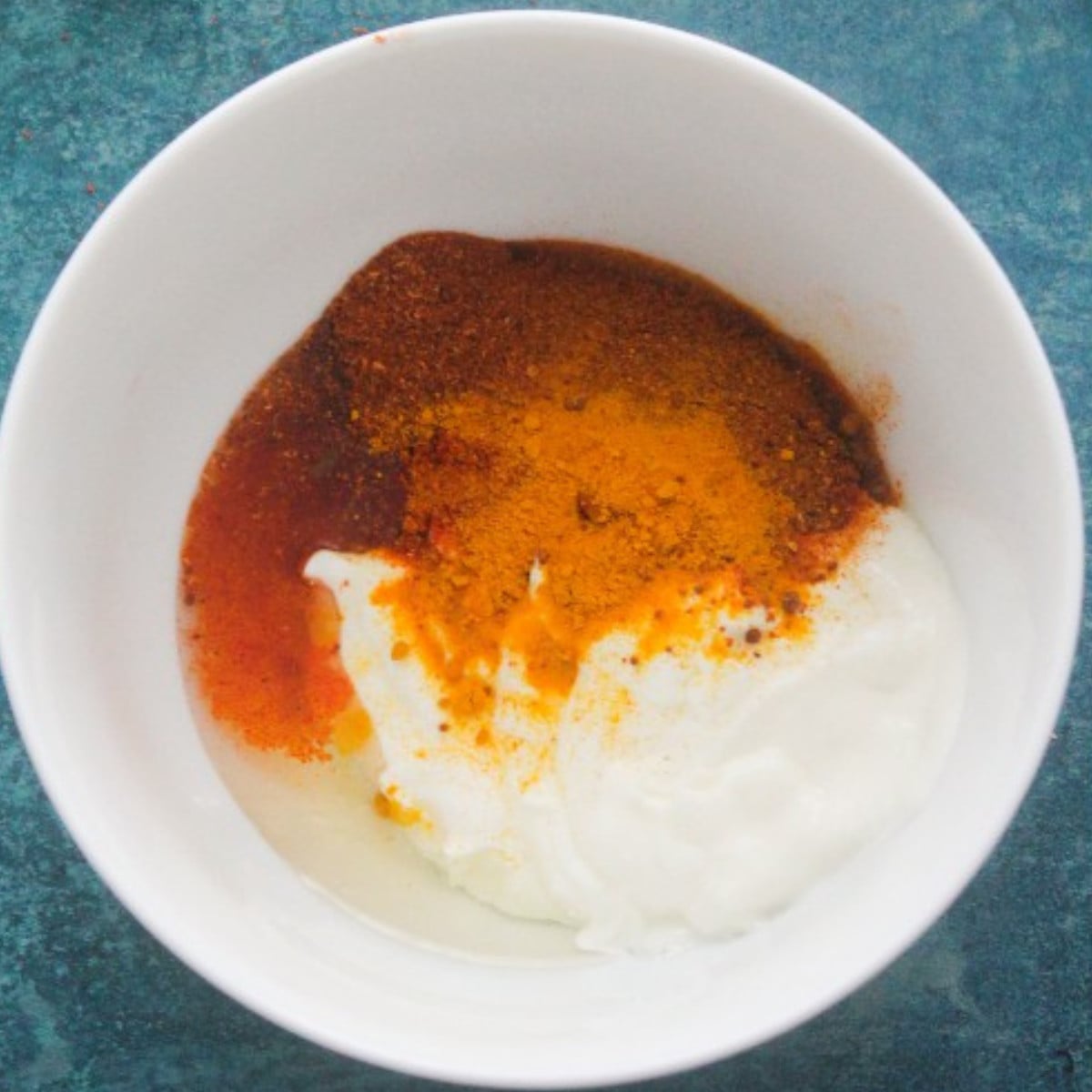 Yogurt, tumeric, cayenne pepper and tandoori in a white bowl.