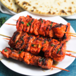 tandoori skewers on a white plate with flat bread in the background on a blue table.