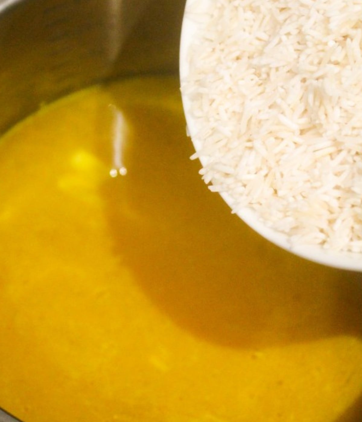 Mixed butter melted, garlic, turmeric, chopped onions, water and rice poured into a silver pot.