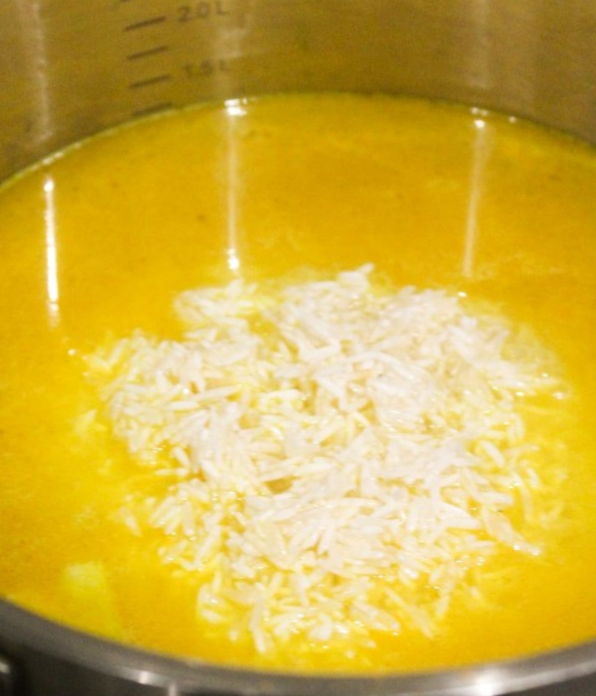 Mixed butter melted, garlic, turmeric, chopped onions, water and white rice in a silver pot.