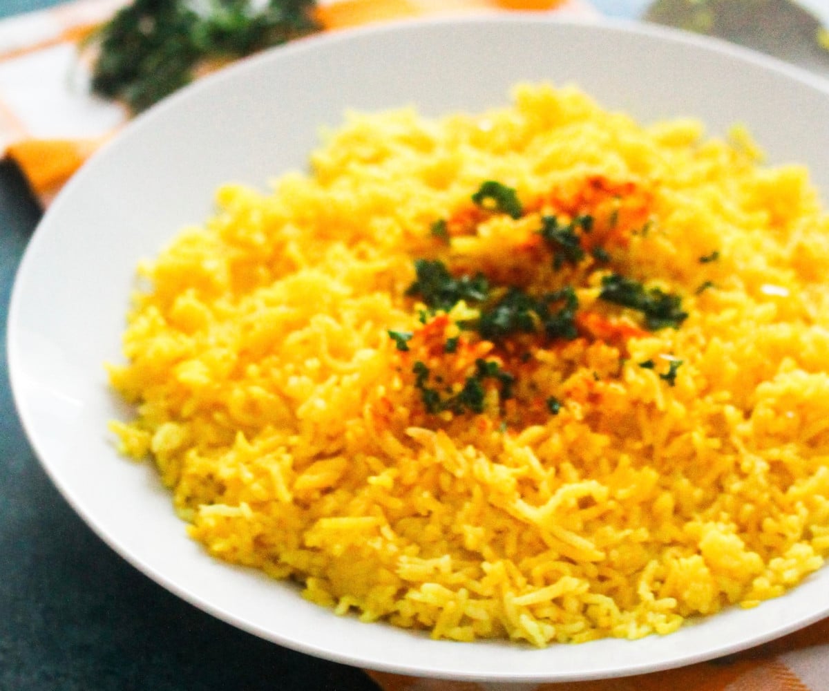 Yellow rice with paprika and fresh herbs in a white bowl.