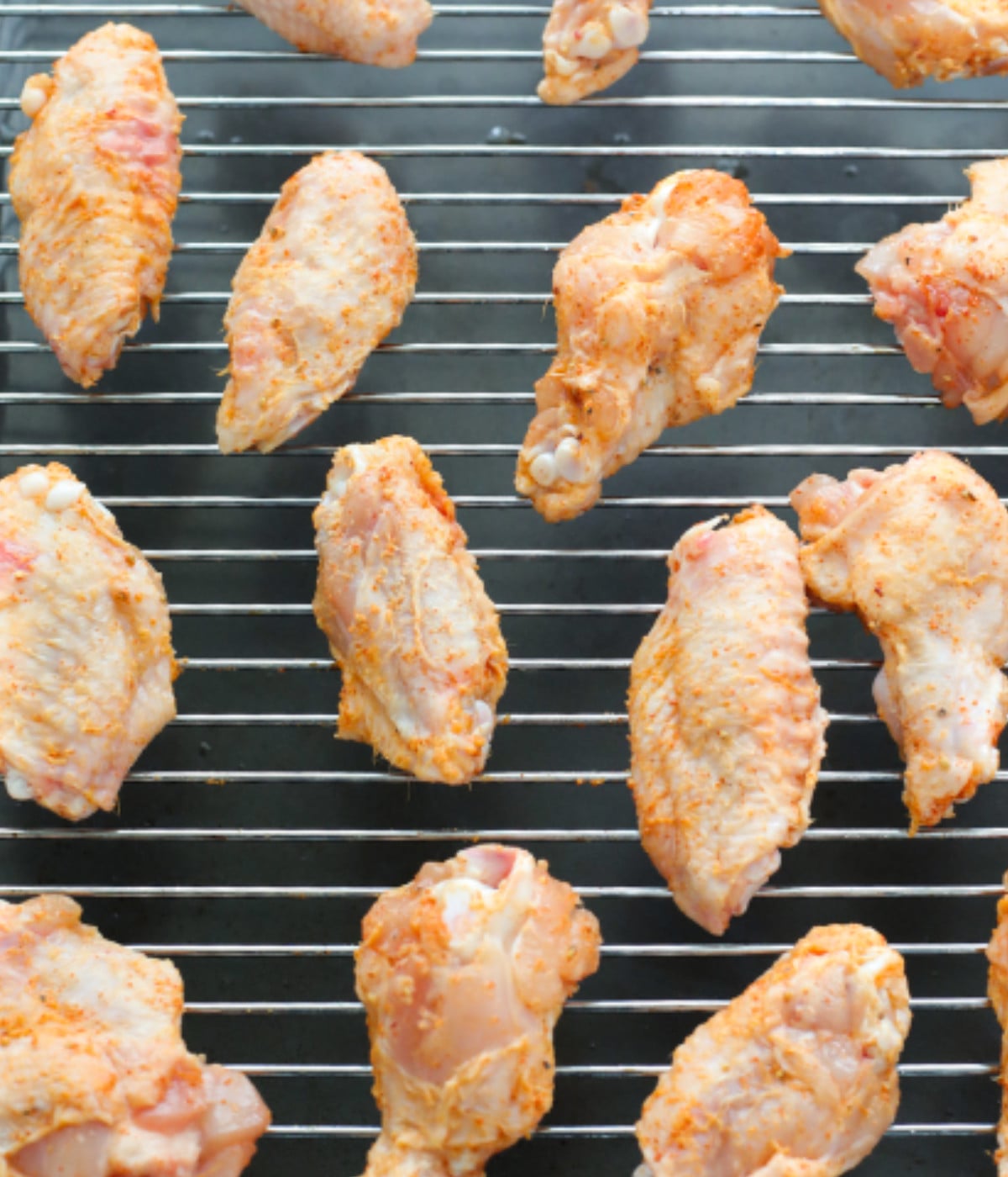 Seasoned chicken wings on an oven rack.