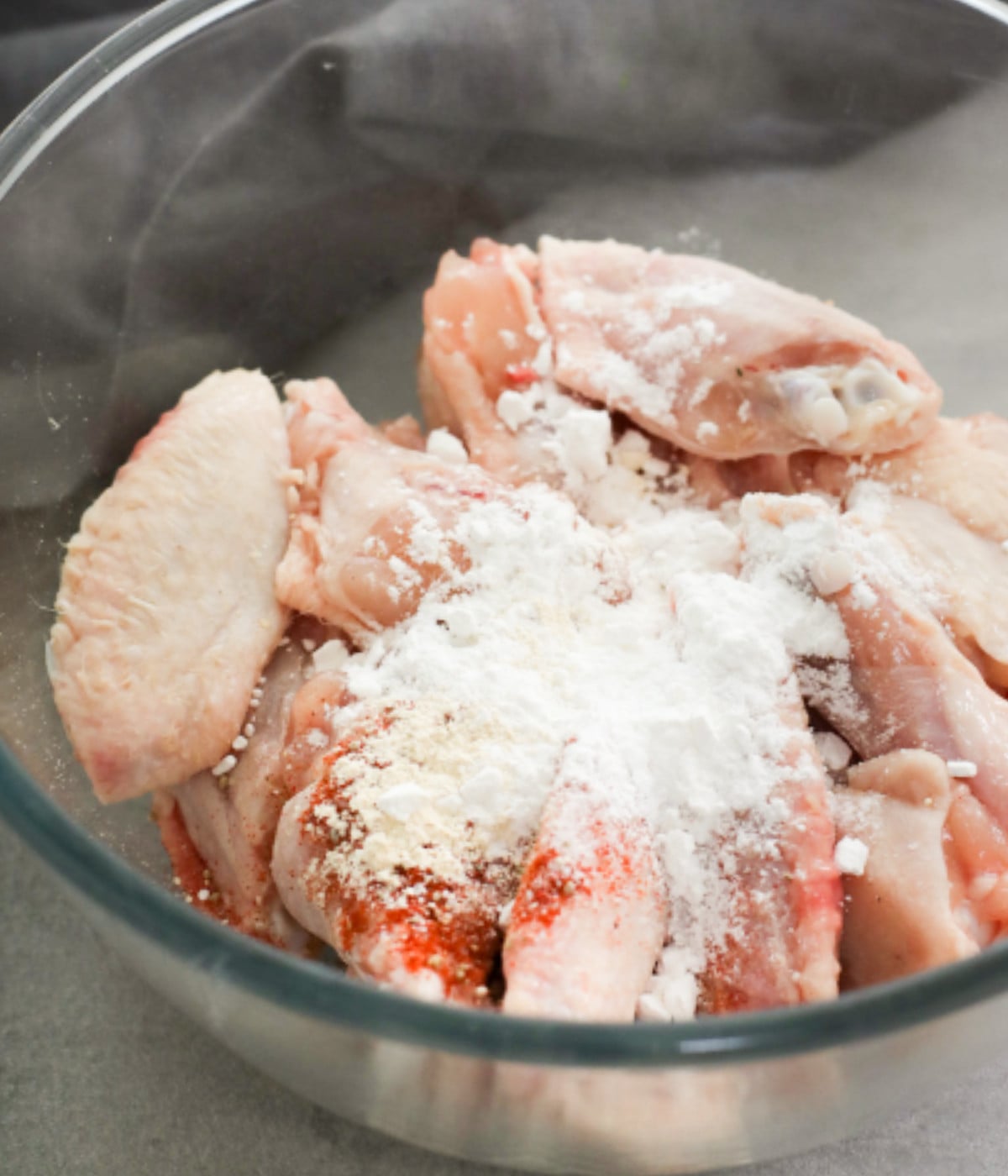Uncooked chicken wings, baking powder, salt pepper in a glass bowl.