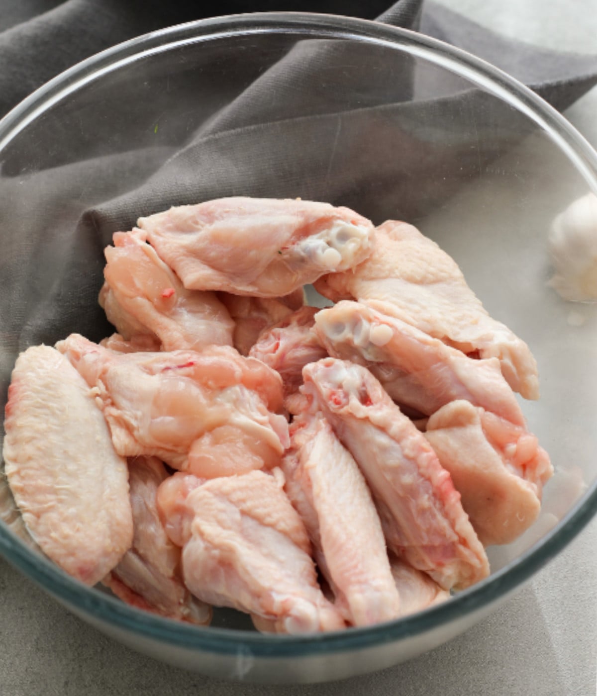 Uncooked chicken wings in a glass bowl.