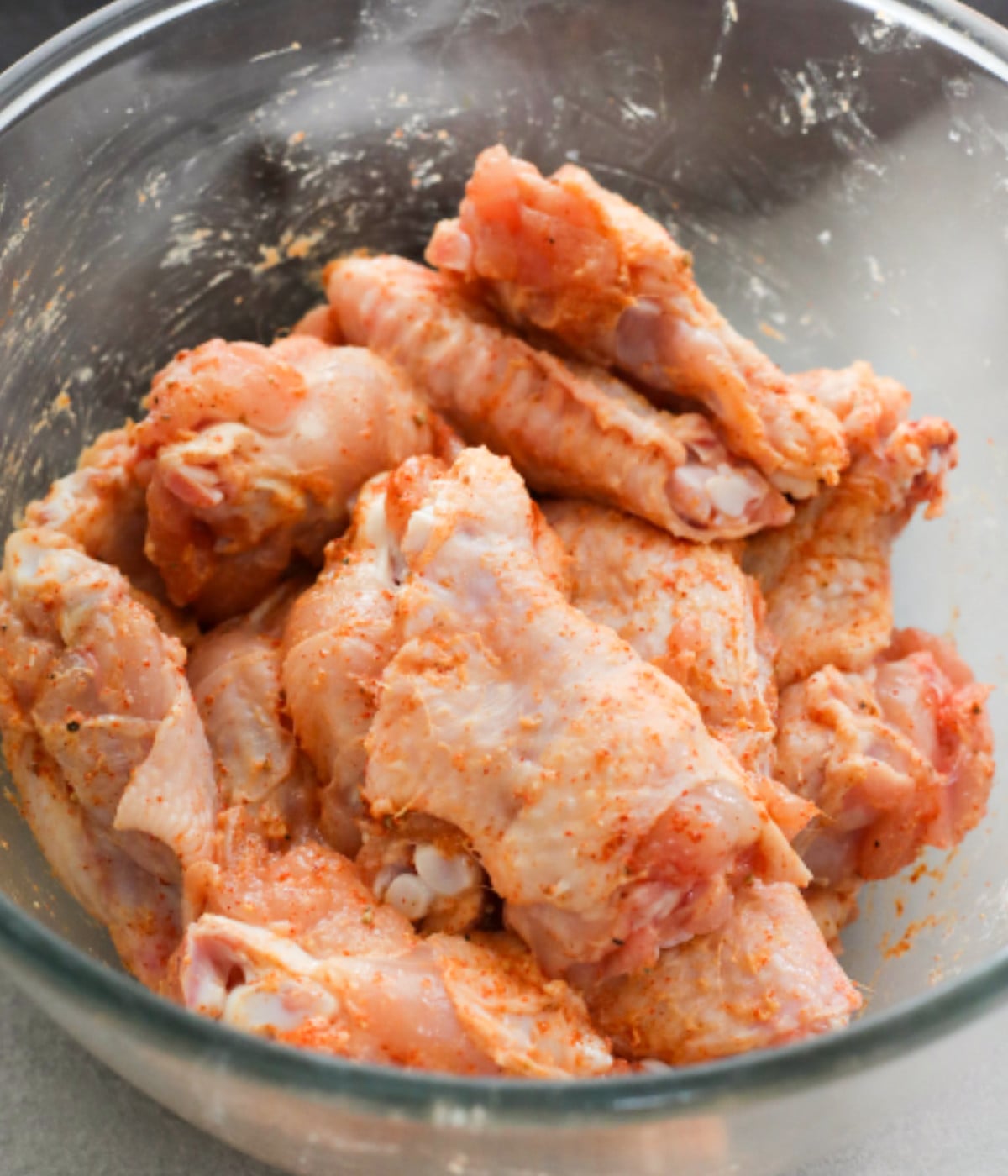 Uncooked chicken wings mixed with baking powder, salt pepper in a glass bowl.