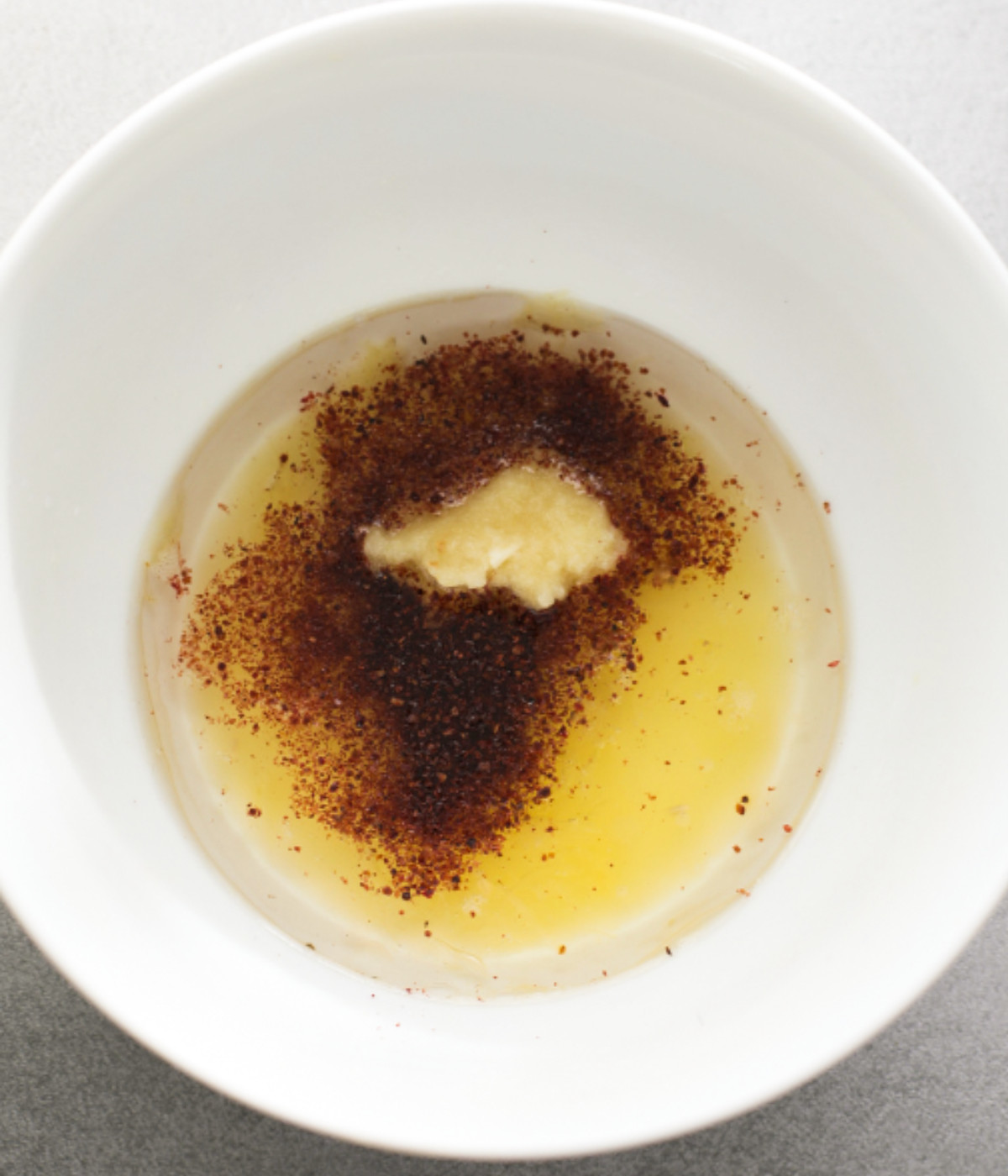 Oil, garlic, sumac and lemon juice in a white bowl.
