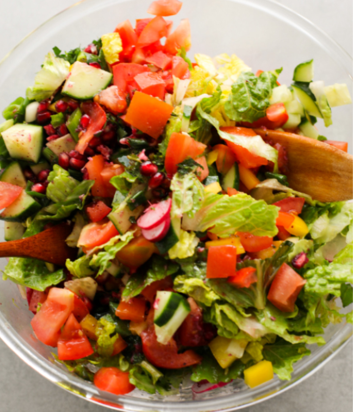 Tomatoes, cucumber, pomegranates, lettuce and yellow peppers tossed in a glass bowl.