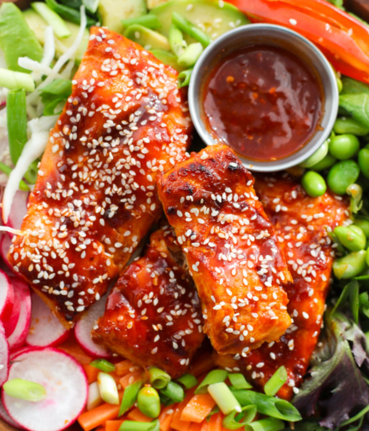 Spicy salmon, red peppers, edamame beans, radish, avocado, carrots and cabbage in a bowl.