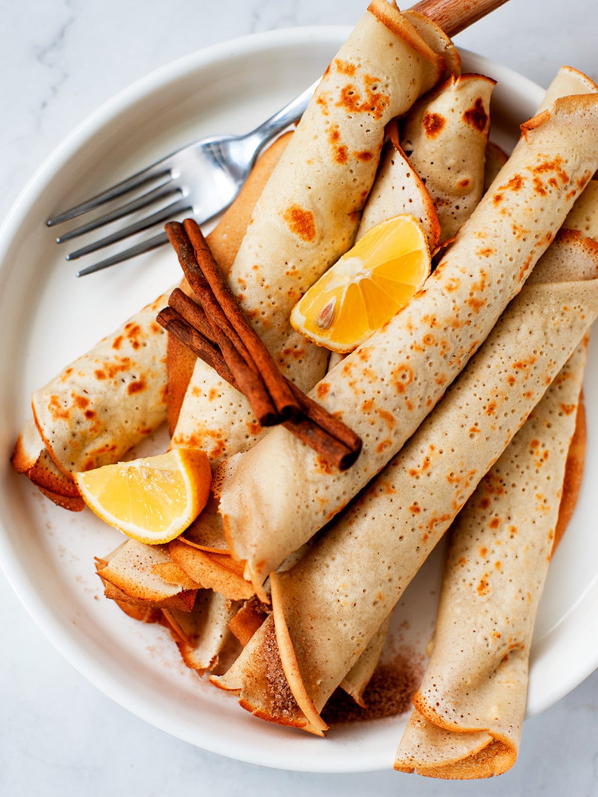 African Pancakes on a plate with lemon wedges and cinnamon sticks with fork.