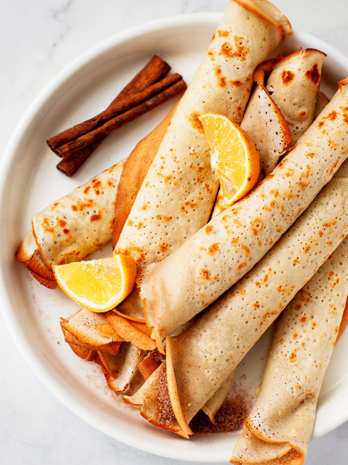 African Pancakes on a plate with lemon wedges and cinnamon sticks.