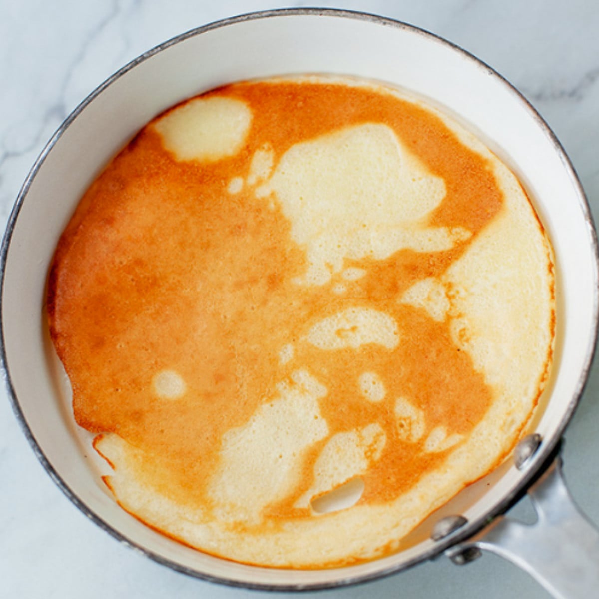 African pancake batter flipped in a white pan.