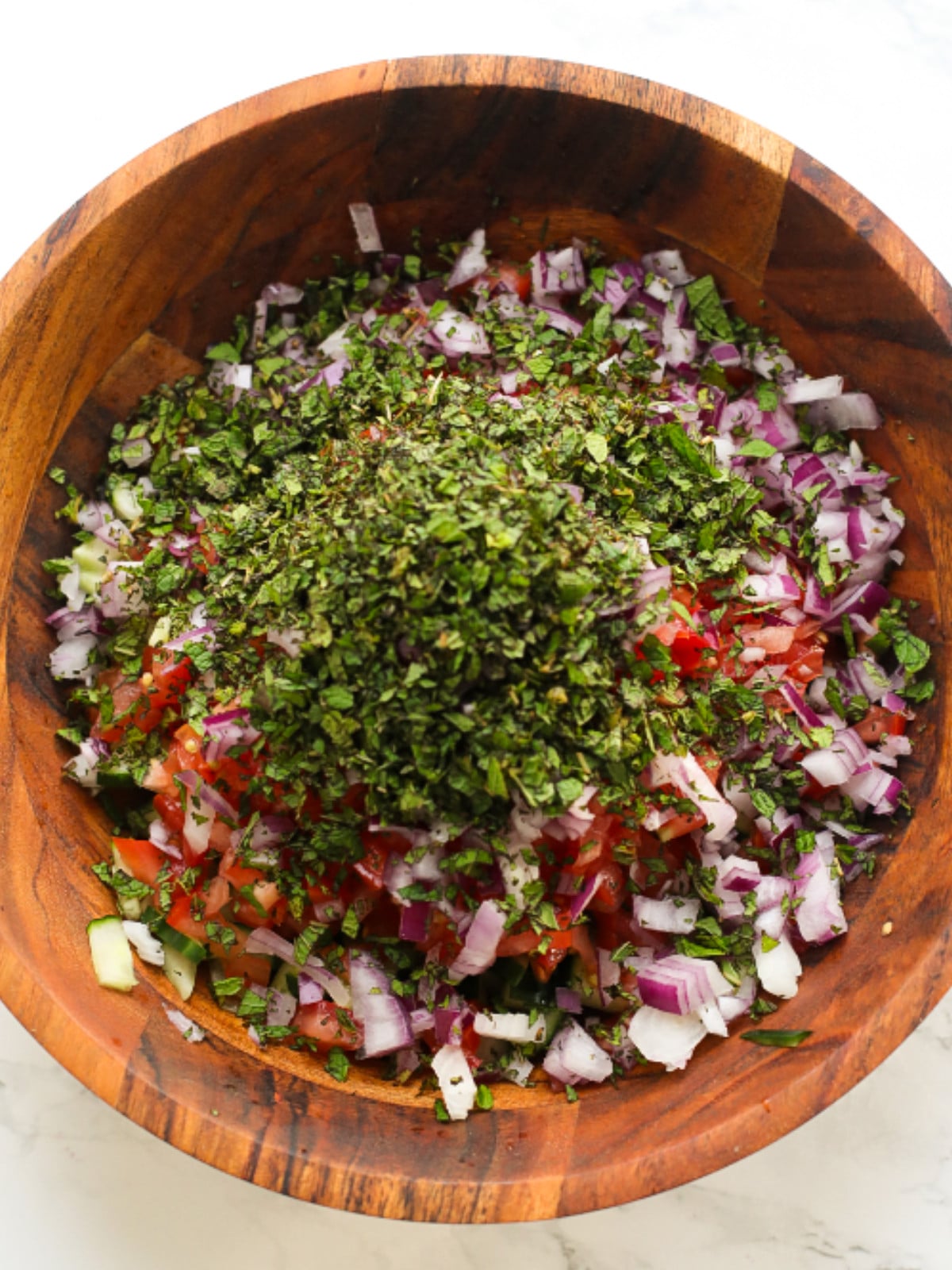 Chopped tomatoes, red onions, cucumbers and mint in a wooden bowl.