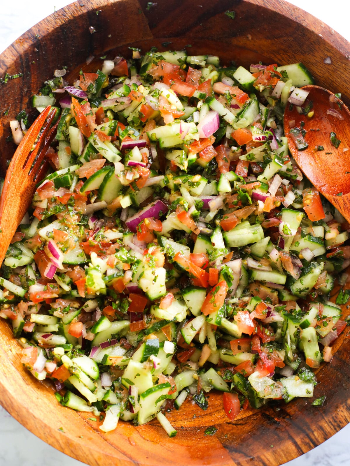Chopped tomatoes, red onions, cucumbers and mint mixed in a wooden bowl.