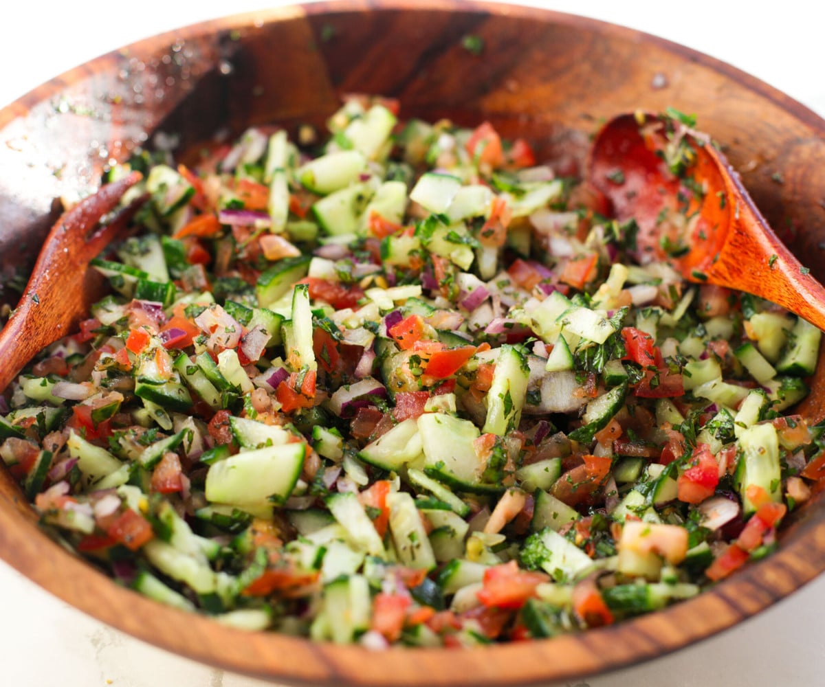 Cucumber, tomato, red onion, mint and oil tossed in a wooden bowl.