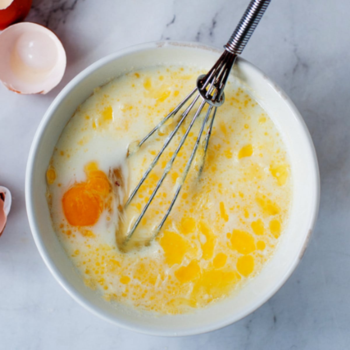 Eggs and milk whisked in a white bowl.