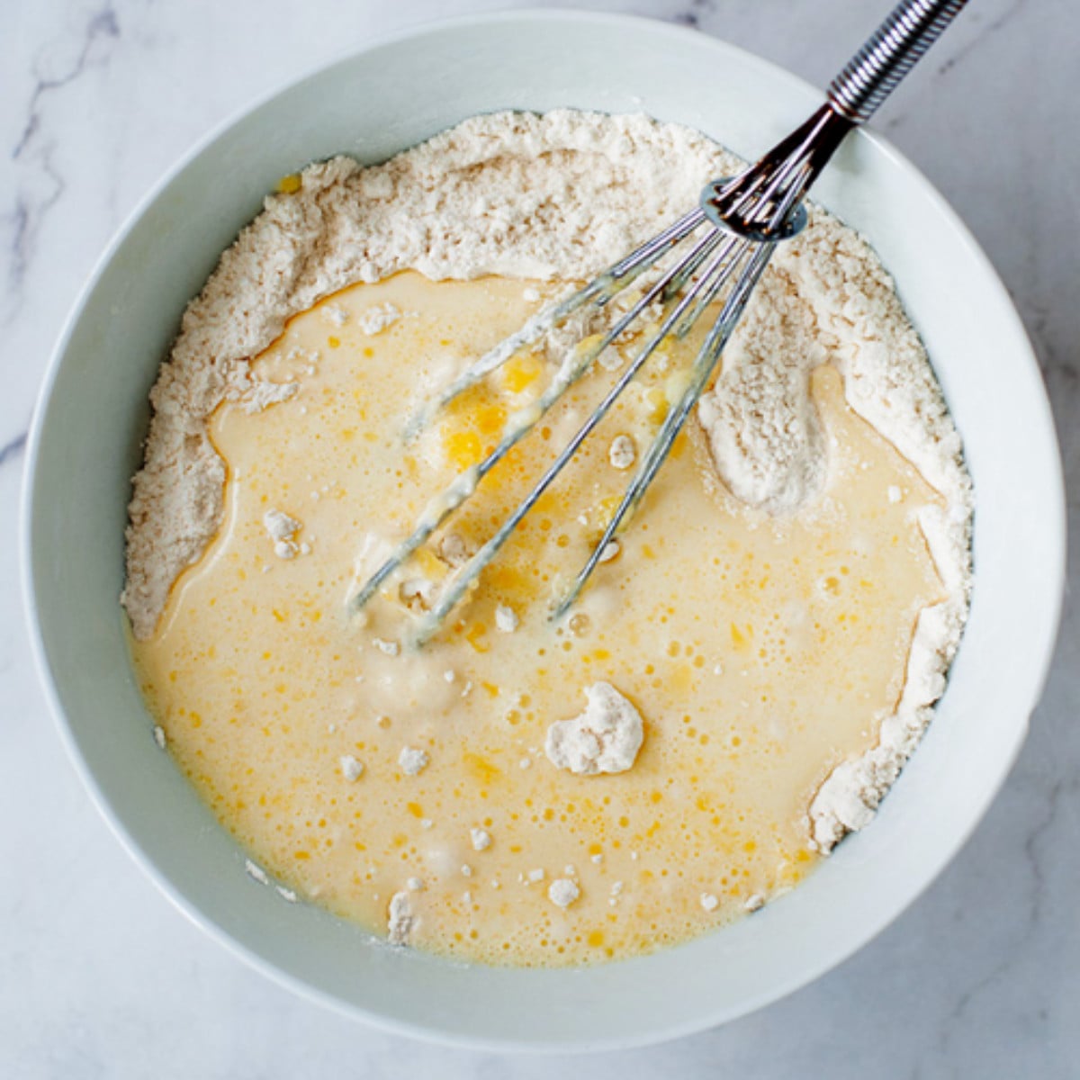 Flour, eggs and milk whisked in a white bowl.