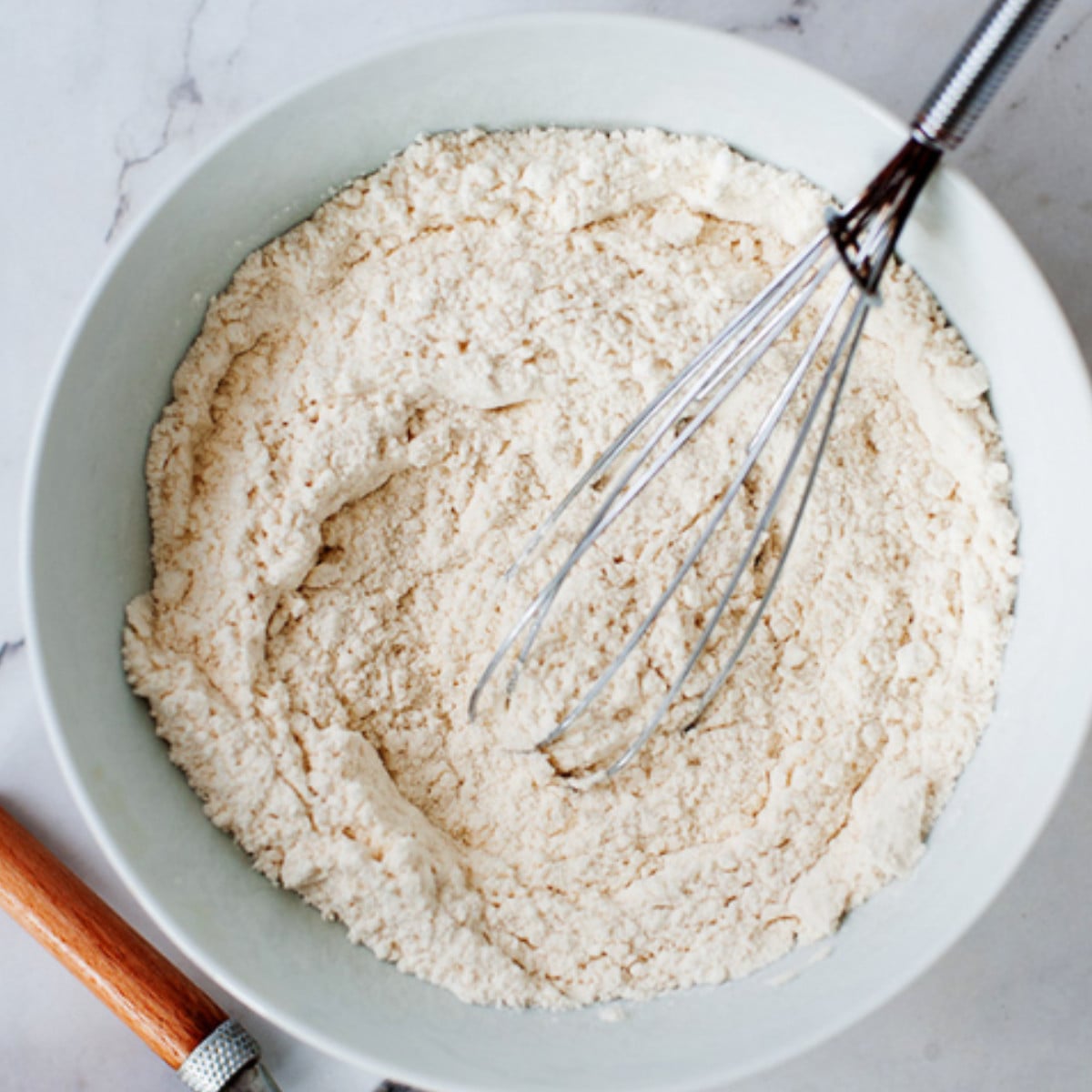 Flour mixture in a white bowl with a silver whisk.