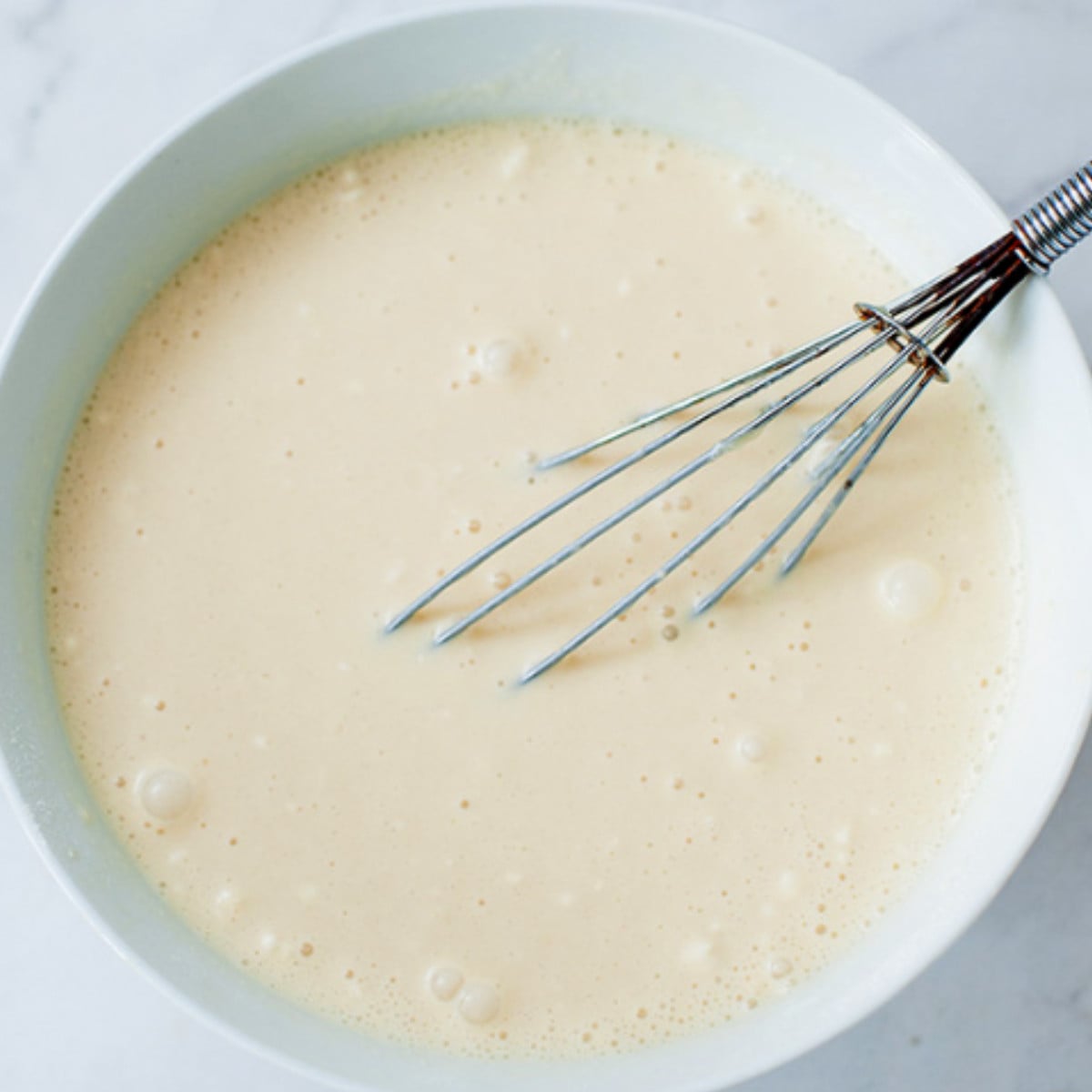 Pancake batter whisked in a white bowl.