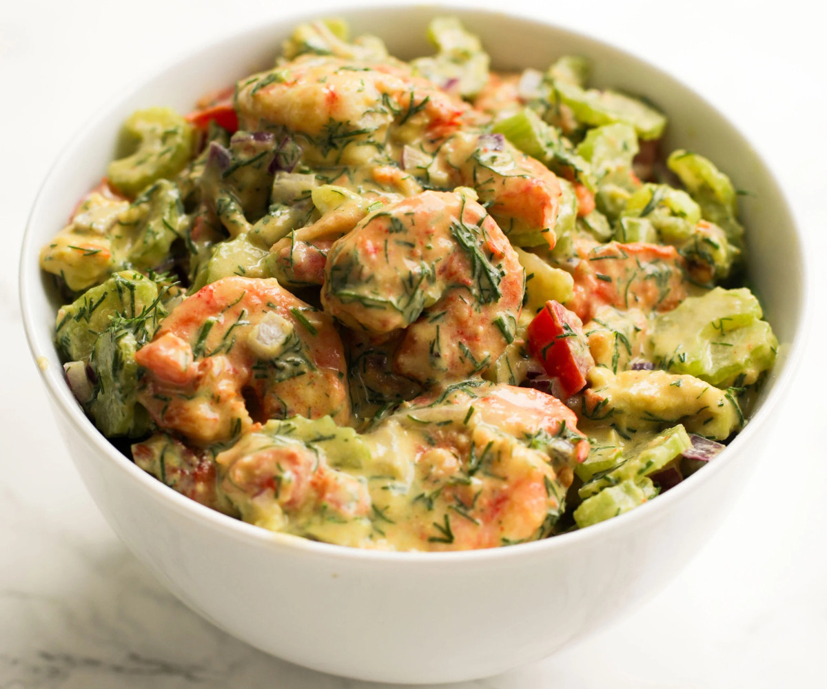 Shrimp, avocado, celery, dill, red onions and tomatoes mixed in a bowl.