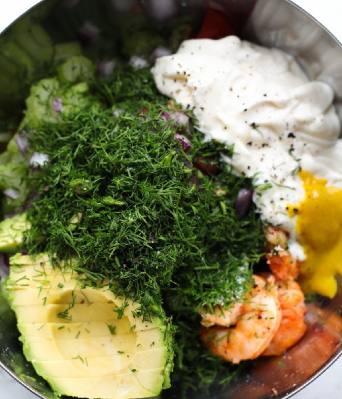Shrimp, dill, avocado, red onions, tomatoes, mayonnaise, mustard and celery in a bowl.