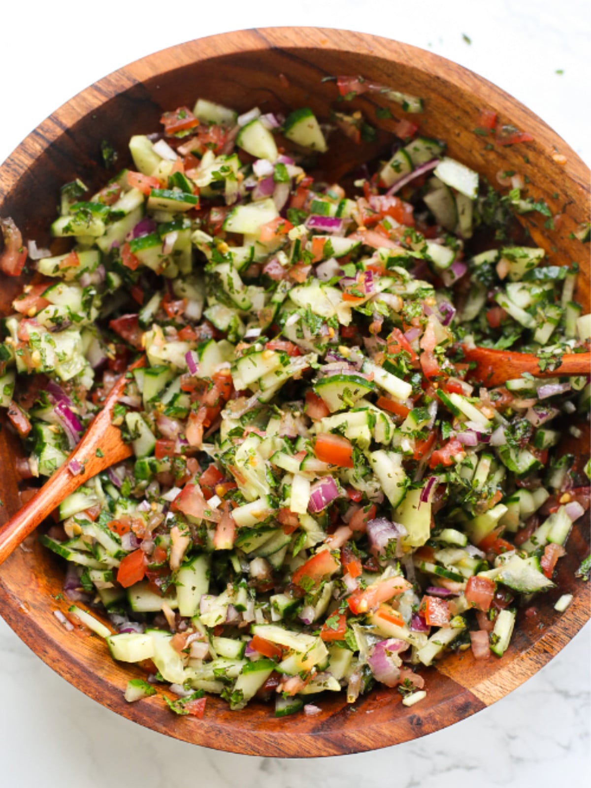 Tossed chopped tomatoes, red onions, cucumbers and mint in a wooden bowl.