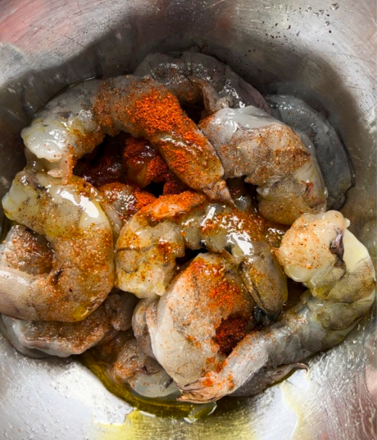 Uncooked shrimp, seasoning and oil in a silver bowl.