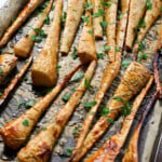 Baked glazed parsnips on a baking tray topped with fresh herbs.