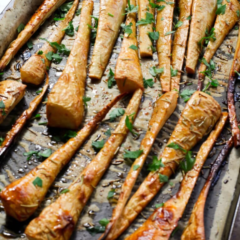Baked glazed parsnips on a baking tray topped with fresh herbs.