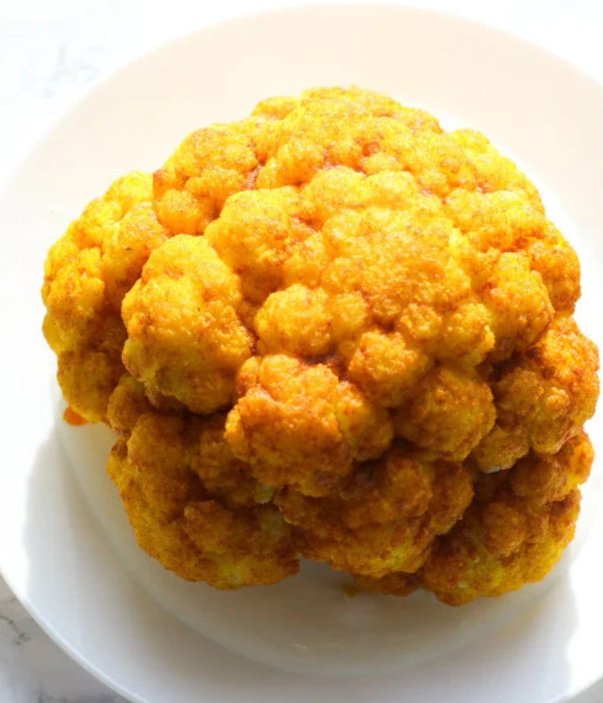 Baked turmeric cauliflower on a white plate with yogurt dressing underneath.