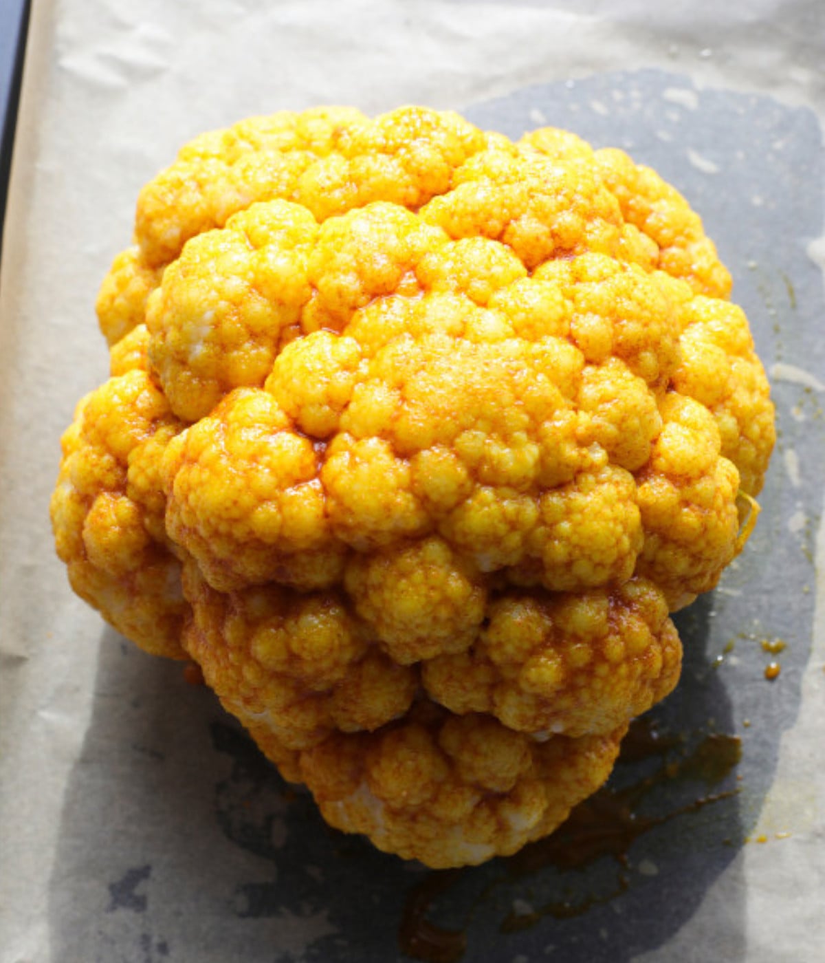 Cauliflower marinated with turmeric seasoning on a lined baking tray.