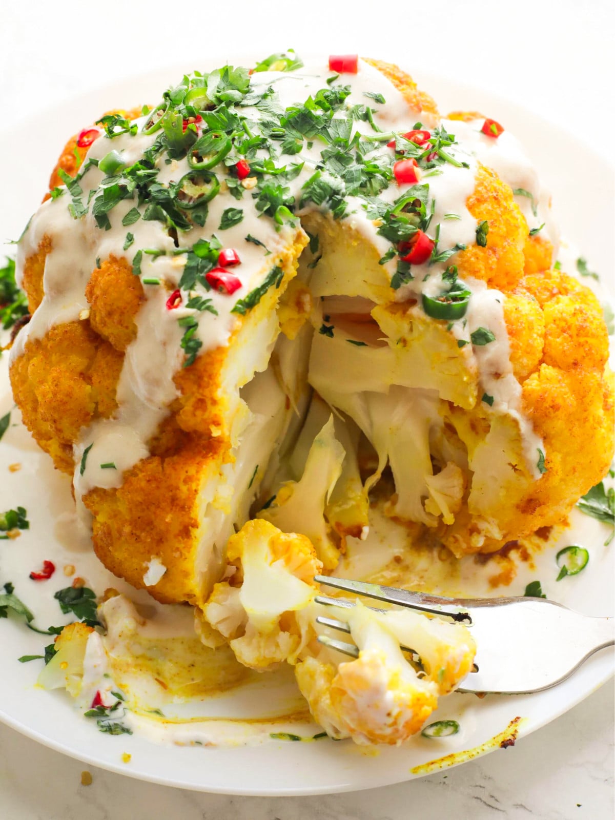 Roasted turmeric cauliflower topped with tahini and chilli dressing on a white plate with a fork.