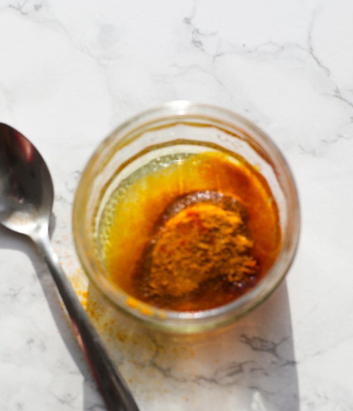 Turmeric, paprika, oil and salt in a small glass bowl. A silver spoon on the table beside it.