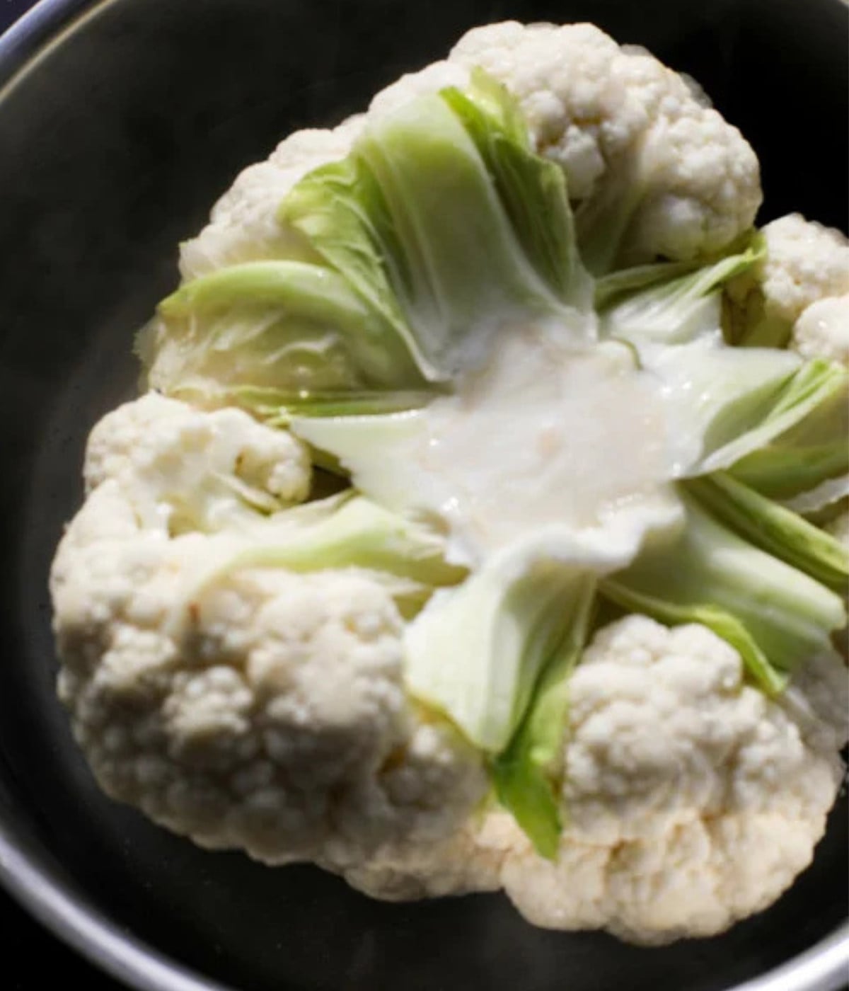 White cauliflower head boiling upside down in a pot of hot water.