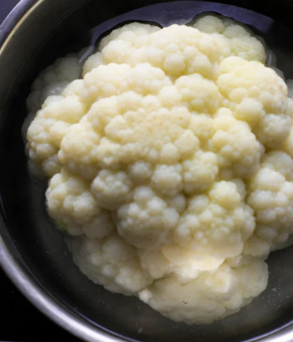 White cauliflower head in a pot of hot water.