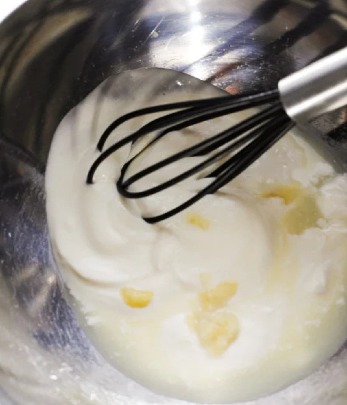 Yogurt, lemon juice and crushed garlic whisked in a silver bowl.
