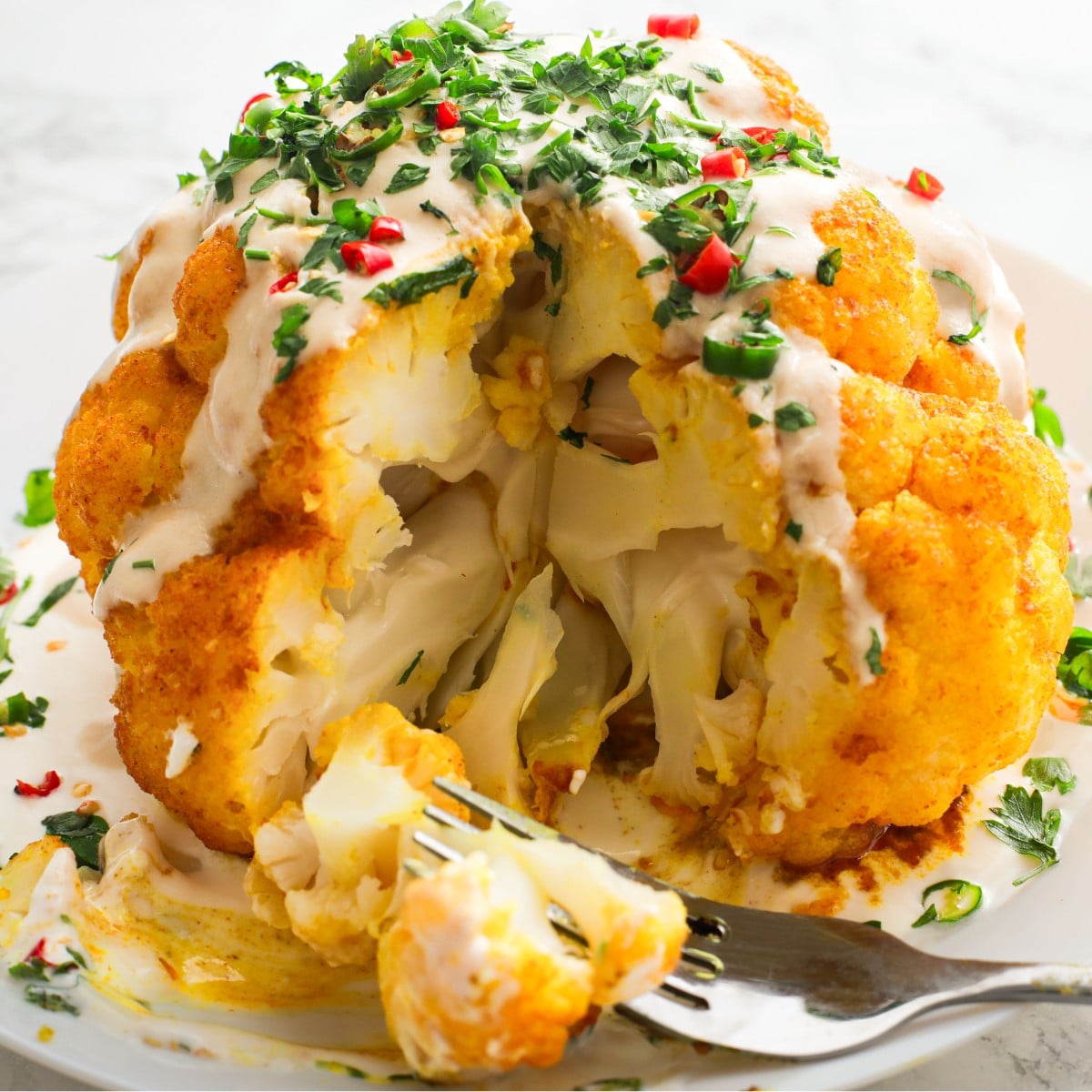 Roasted cauliflower head cut in the middle with yogurt dressing and herbs on top.