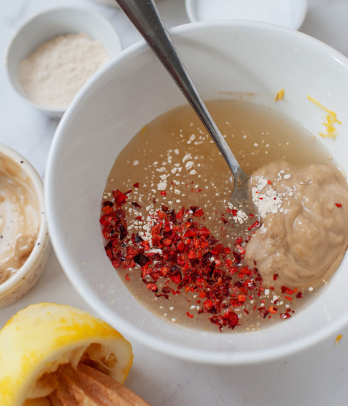 Chilli flakes, lemon juice, tahini and salt mixed in a white bowl.