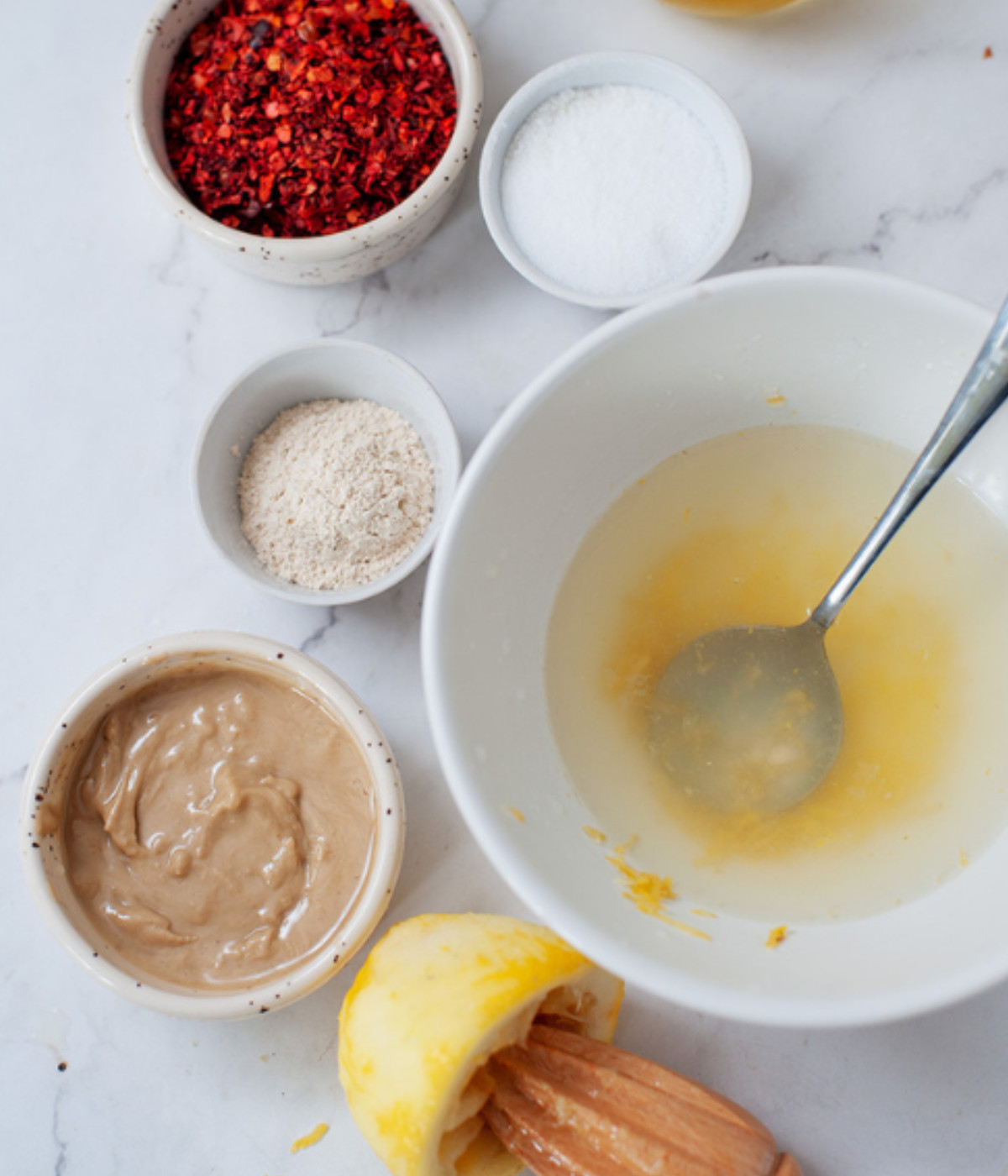 Chilli flakes, lemon juice, tahini and salt on a white table.