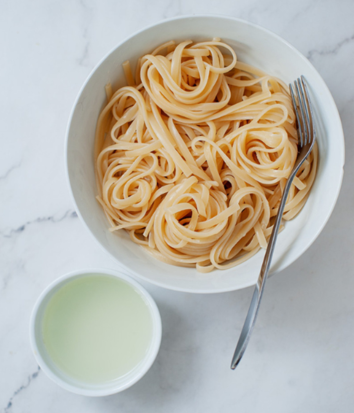 Pasta in a white bowl and pasta water in a small bowl.