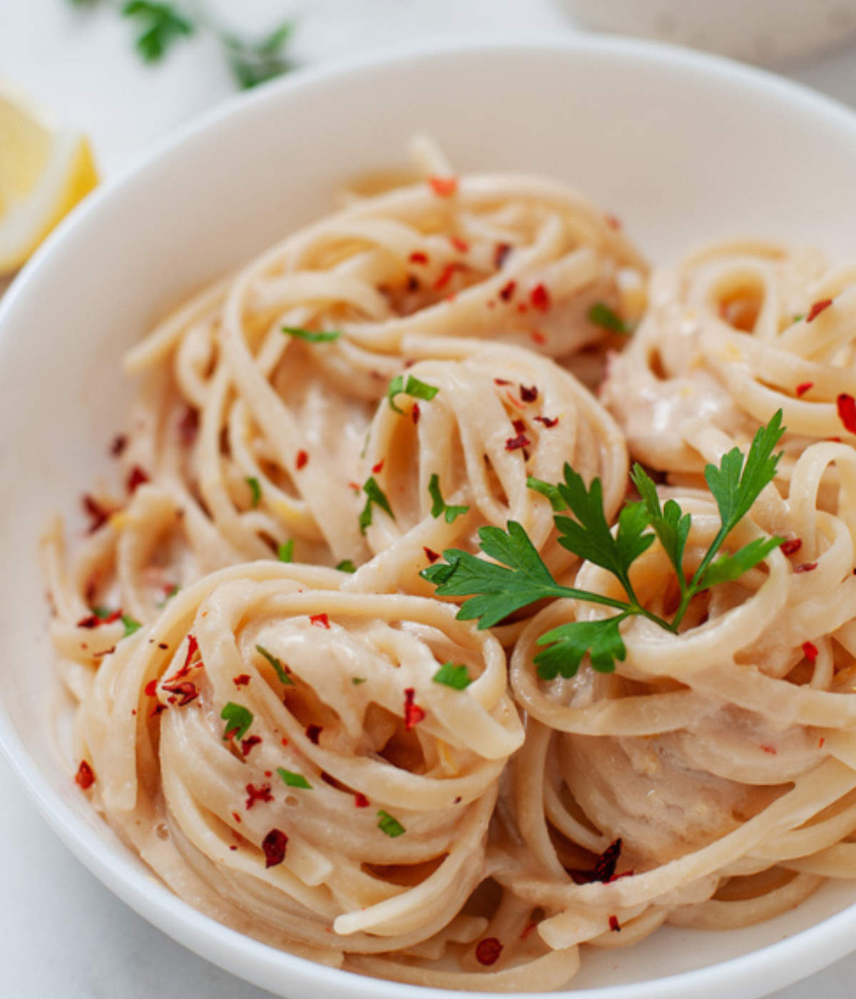Tahini linguine in a white plate garnished with chili flakes and herbs.