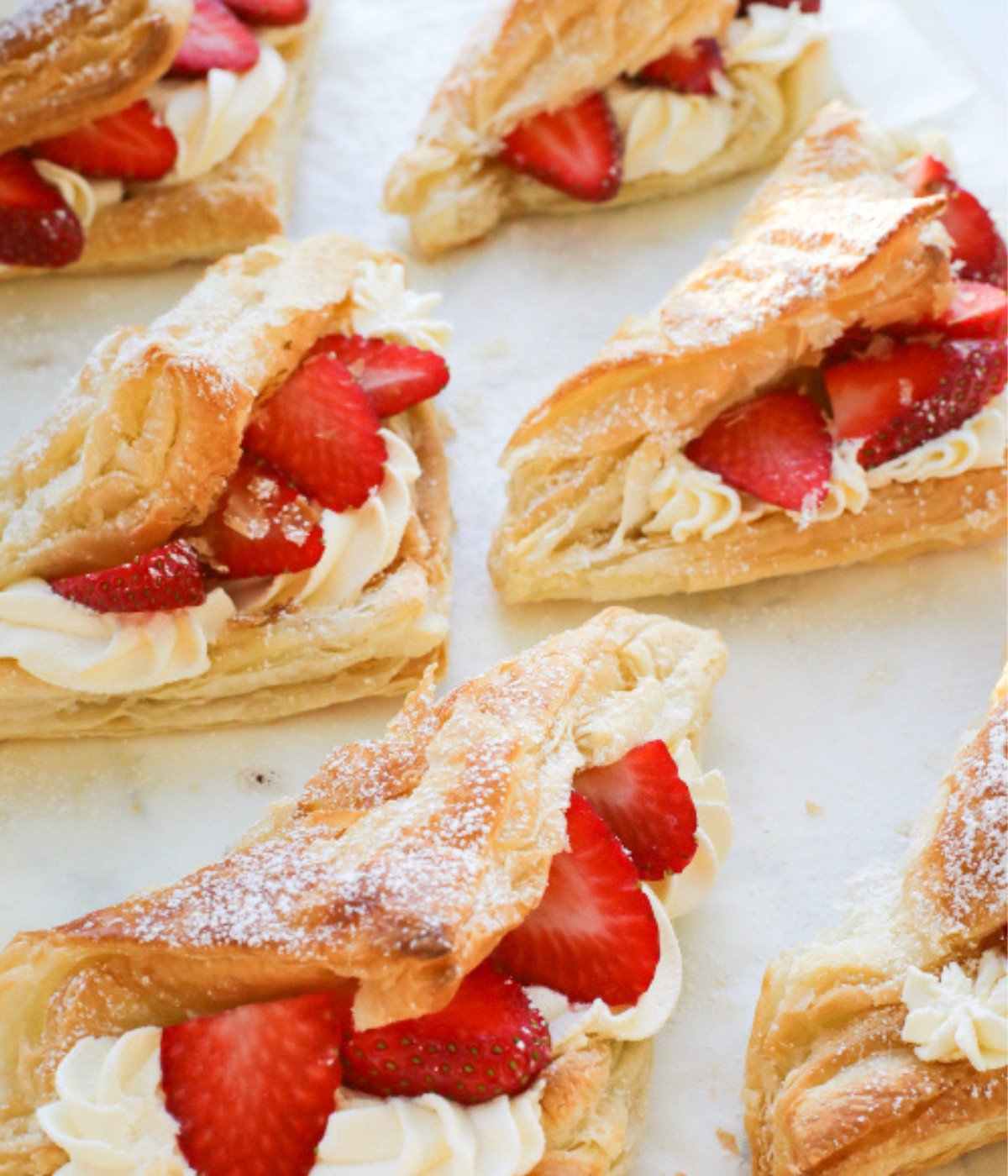 Baked puff pastries shaped like triangles filled with cream and strawberry slices.
