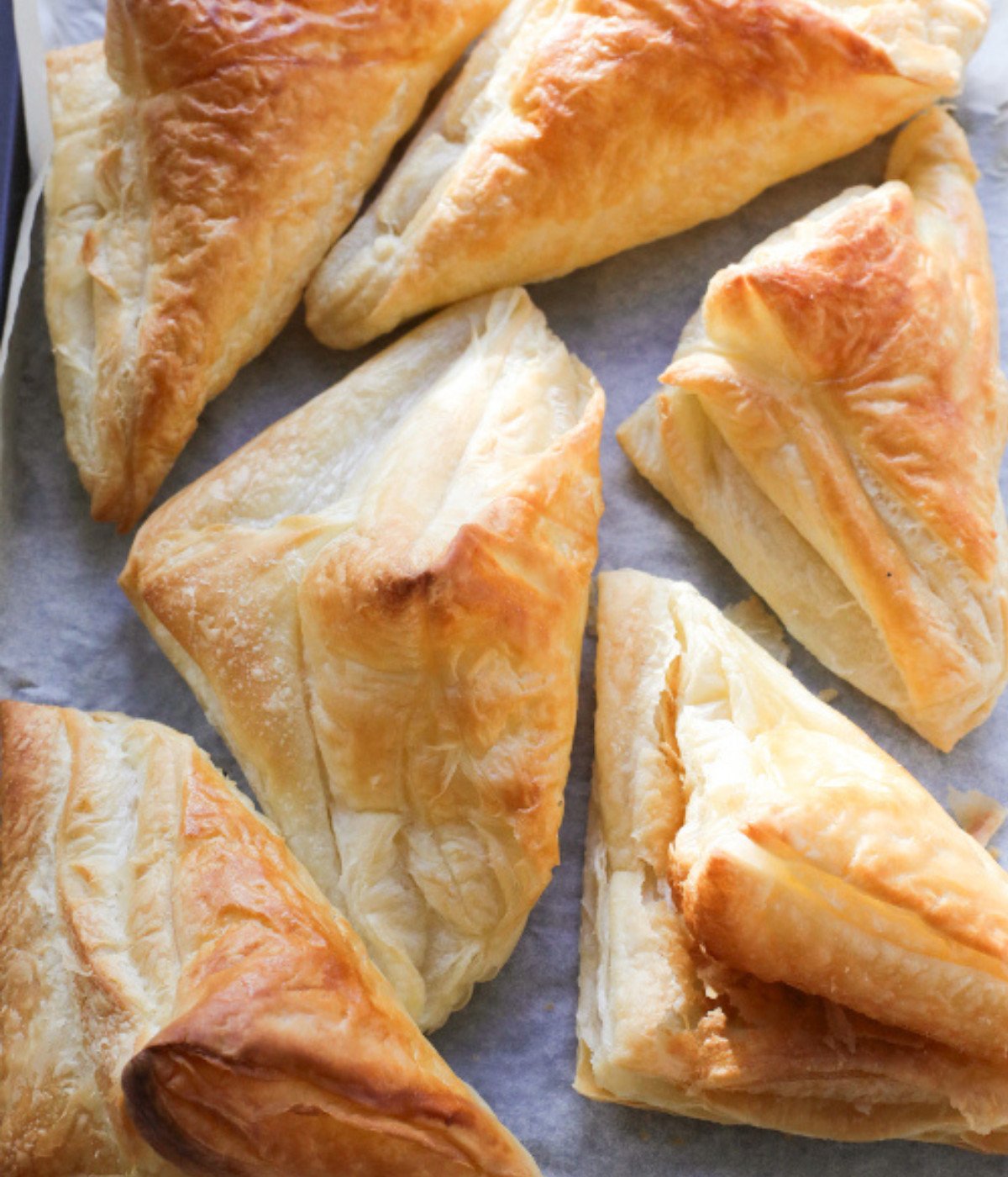 Baked puff pastries shaped like triangles on a lined baking tray.