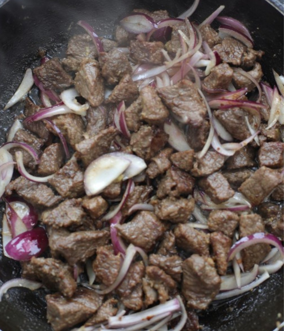 Chopped beef cooking in a black pan with crushed garlic and red onions.