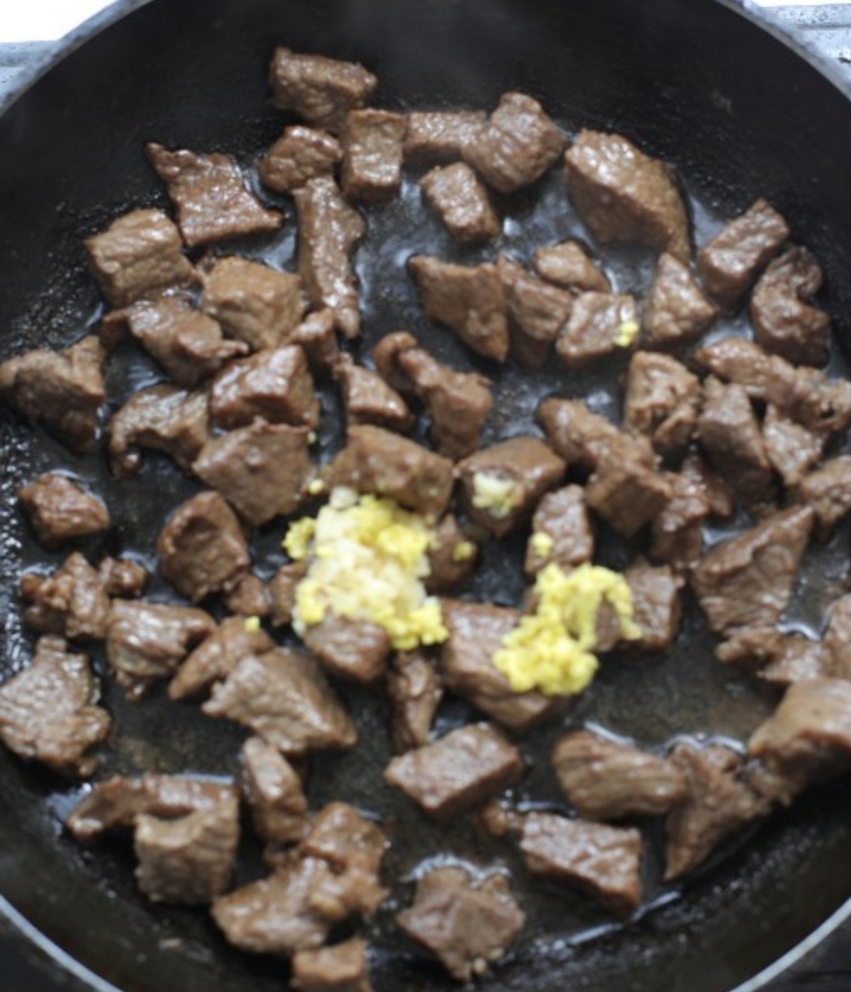 Chopped beef cooking in a black pan with crushed garlic.
