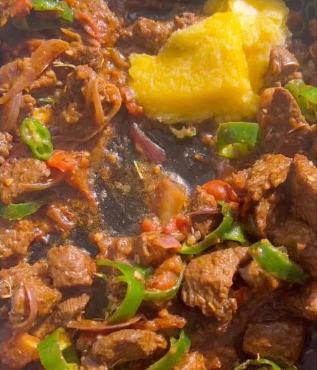 Chopped beef cooking in a black pan with jalapenos and kibbeh.